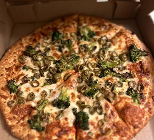 Pizza topped with broccoli and green olives in its box