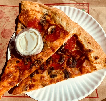 Two pizza slices with pepperoni and mushroom and a cup of garlic dip